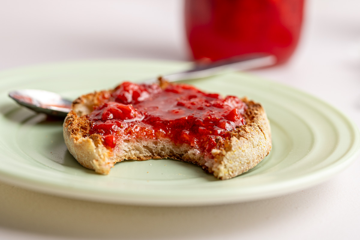 a toasted English muffin topped with strawberry freezer jam with a bite missing.