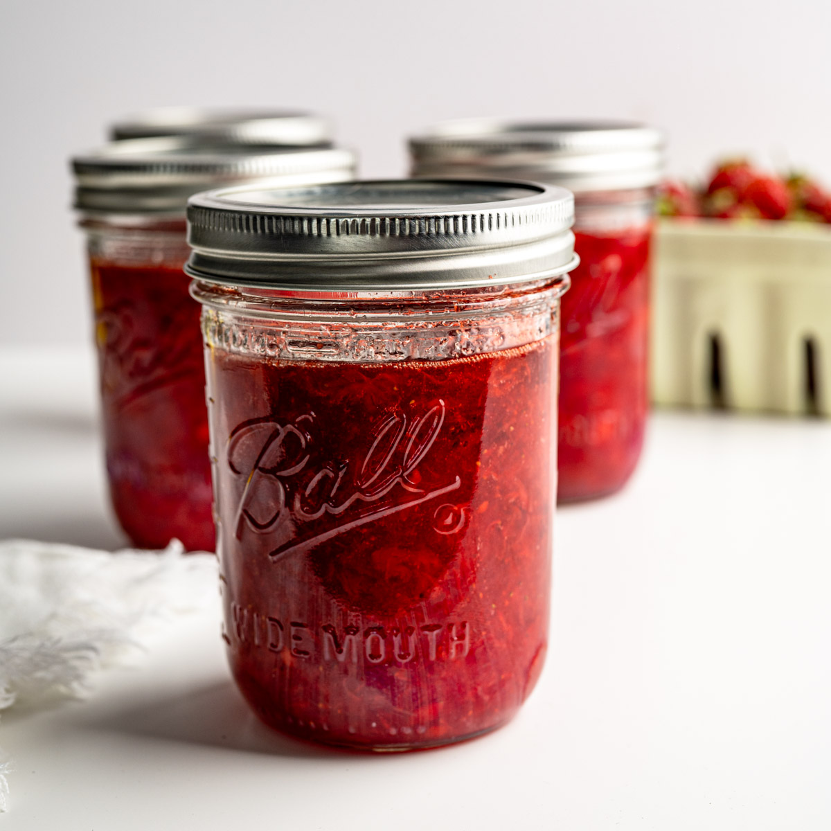four mason jars filled with strawberry freezer jam with fresh berries in the background.