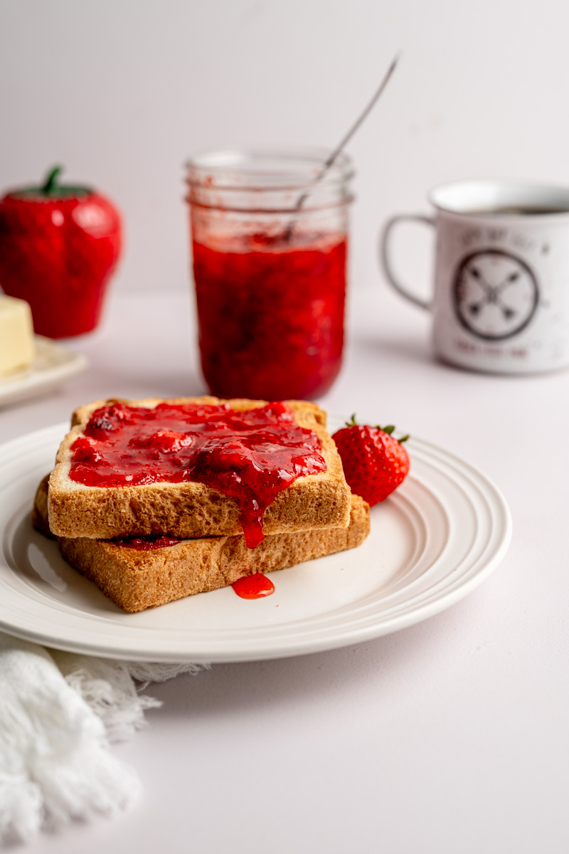 strawberry jam dripping off toasted Texas toast, with a jar in the background.