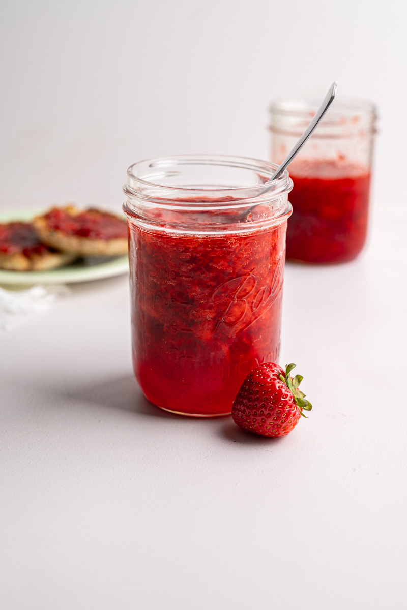 two jars of strawberry freezer jam, with toasted english muffins in the background. 