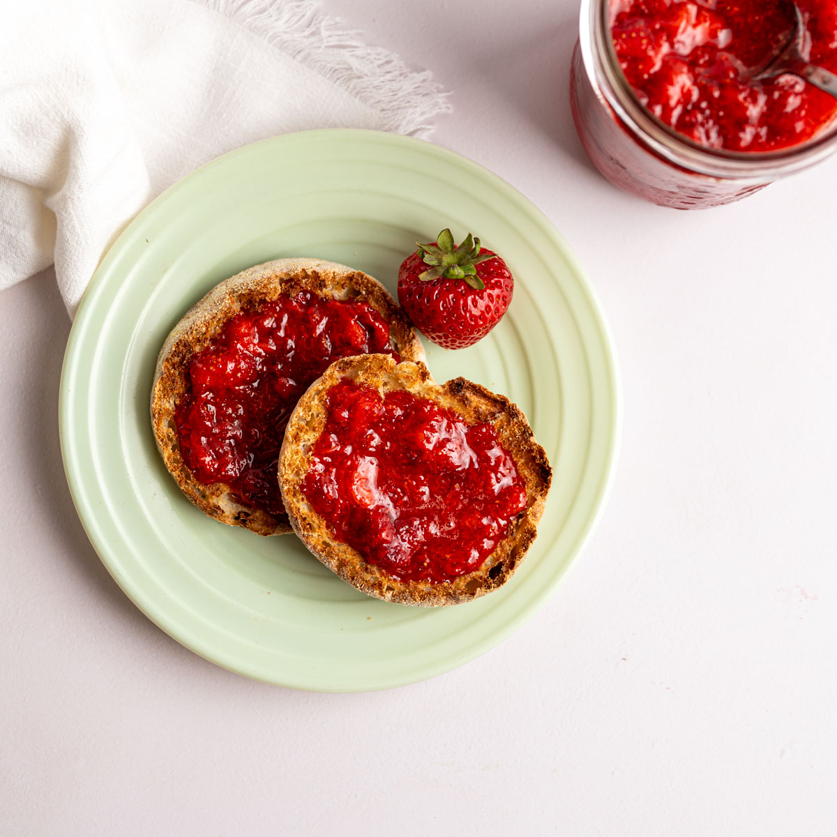 toasted english muffin topped with strawberry freezer jam on a green plate.