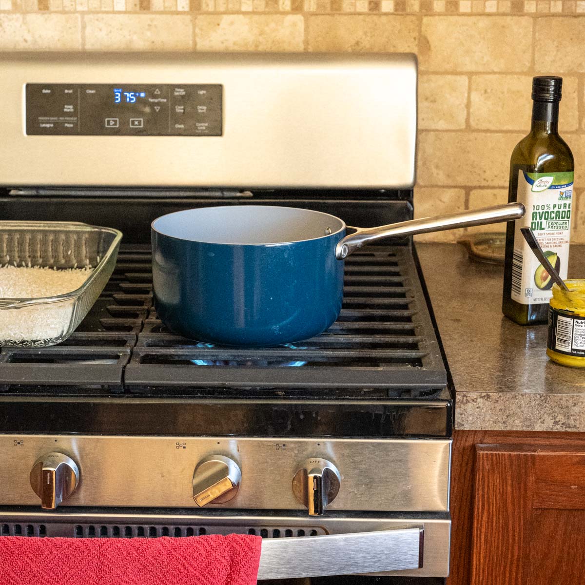 on the stovetop is a blue 3 quart saucepan alongside a 9x13 inche pan filled with uncooked rice.