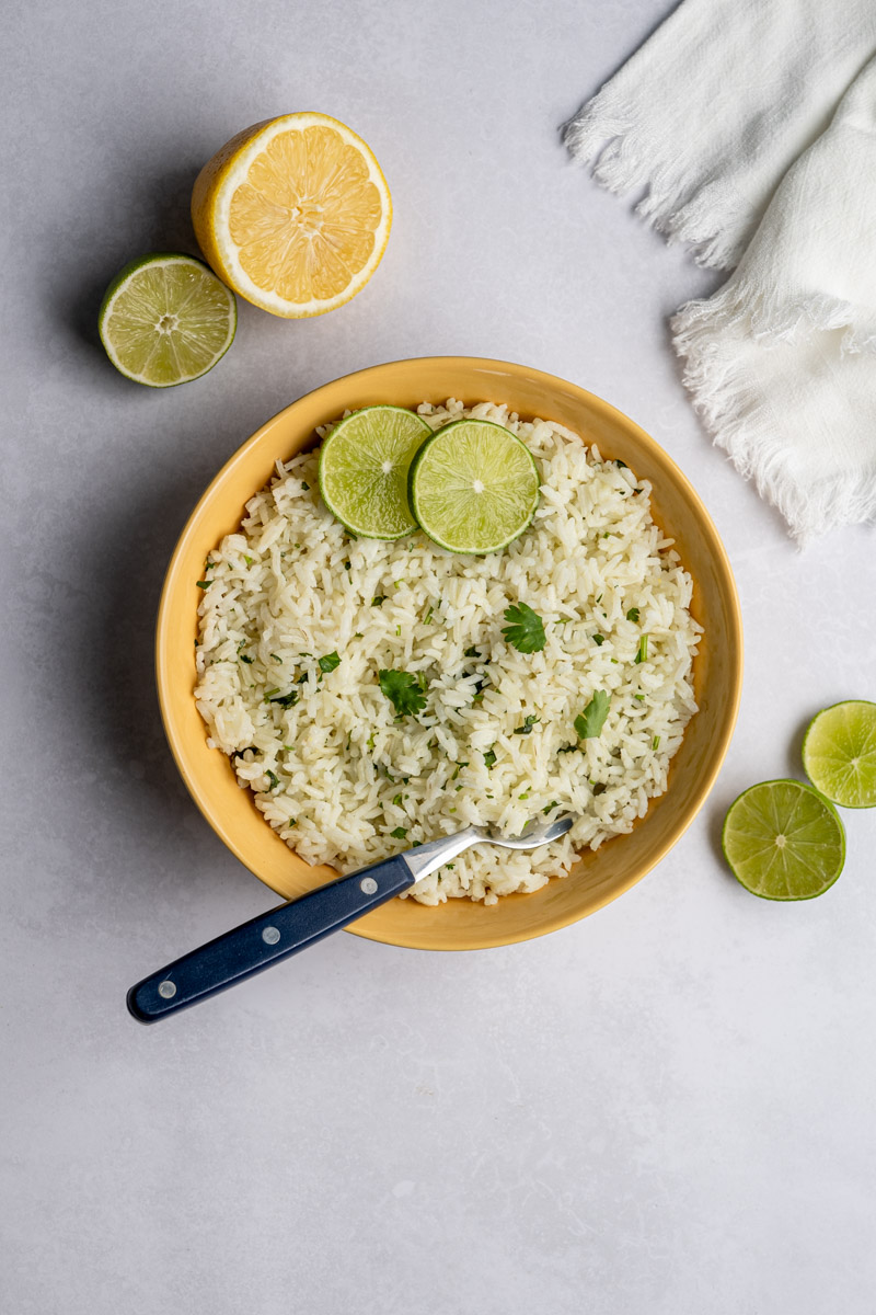 yellow bowl filled with cilantro lime rice topped with lime slices, surrounded by halved lemons and limes.