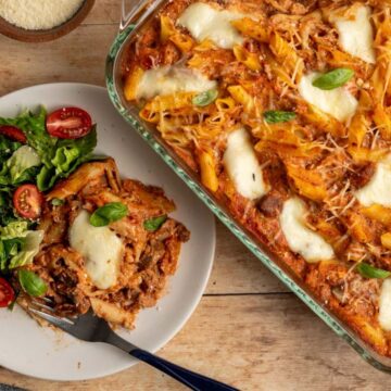 pan of baked ziti alongside a dinner plate with a serving and a side salad.