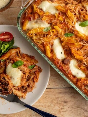 pan of baked ziti alongside a dinner plate with a serving and a side salad.