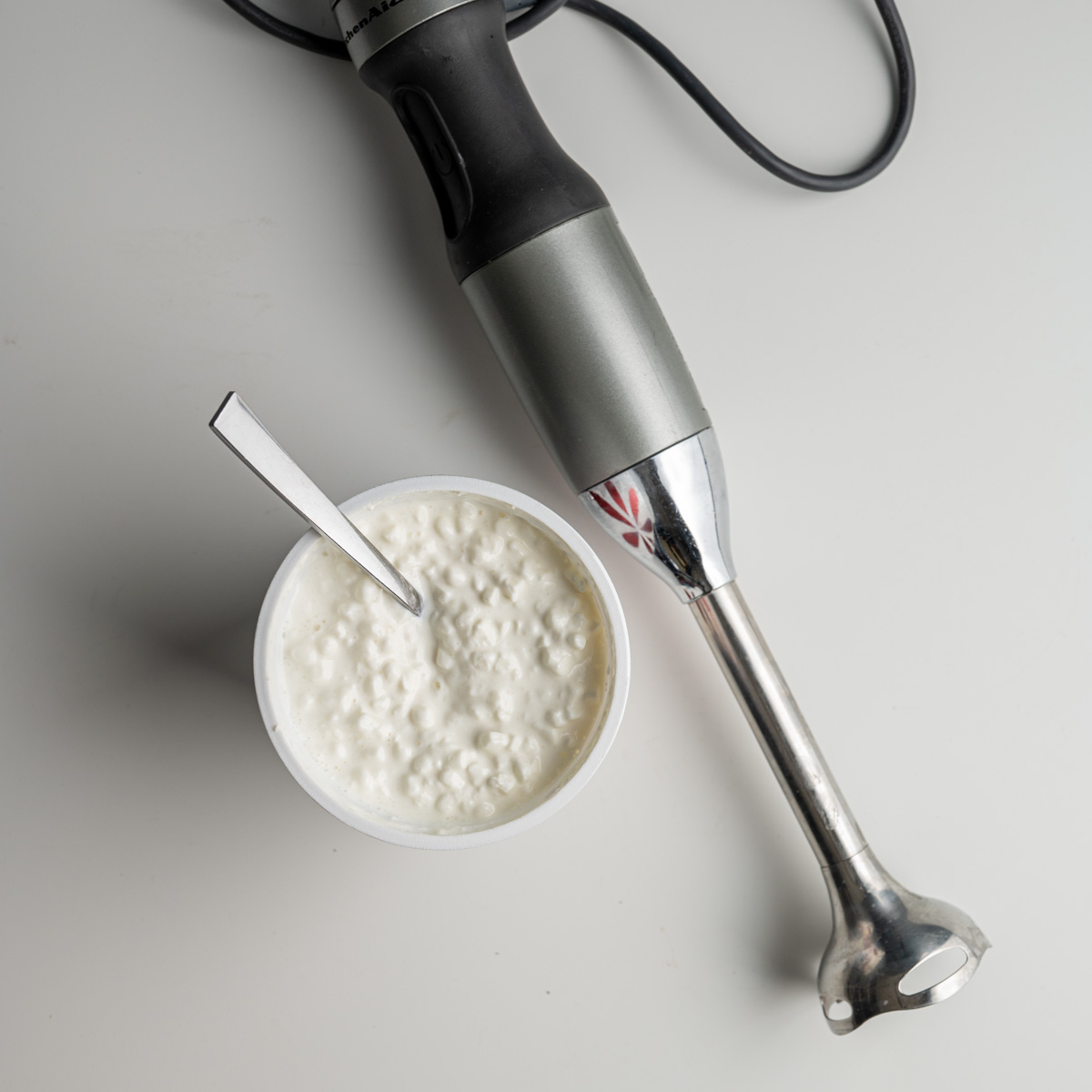 container of cottage cheese next to an immersion blender.