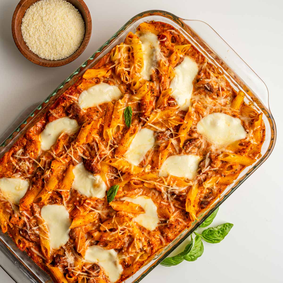 baked ziti with grated parmesan cheese and fresh basil leaves.