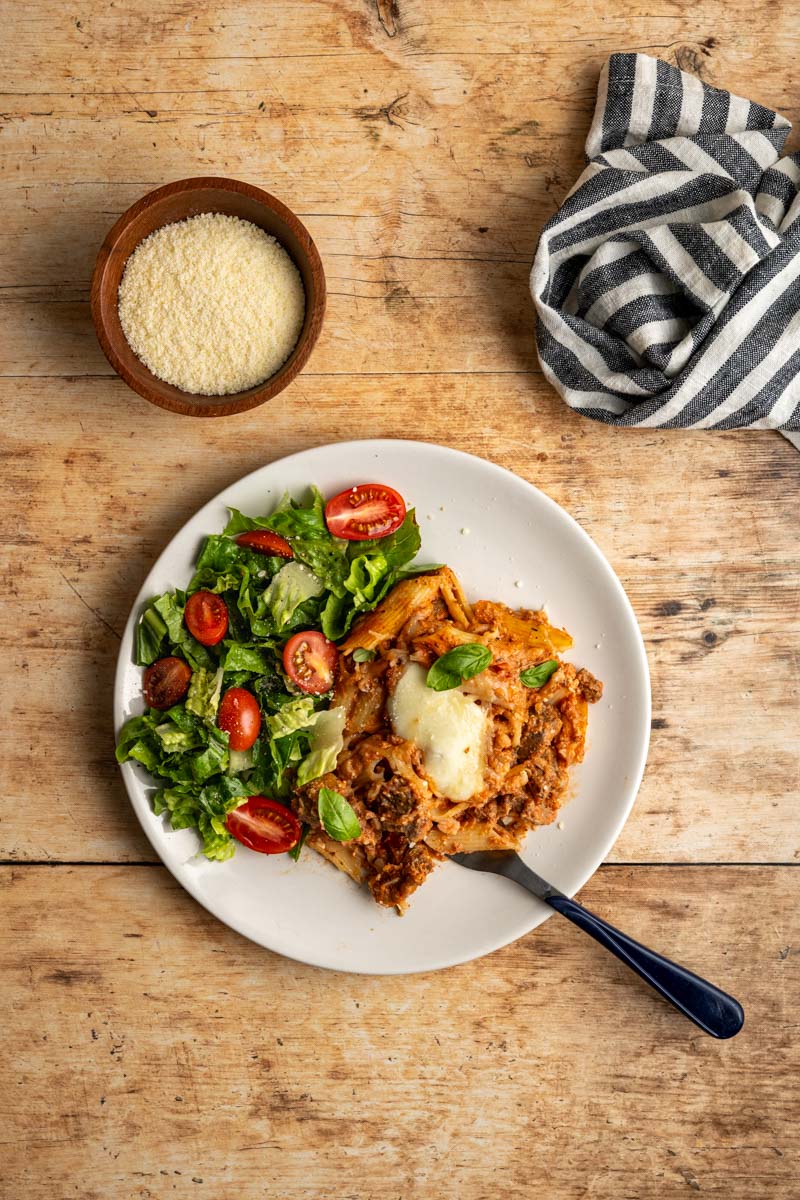 plate with a serving of baked ziti with a side salad.