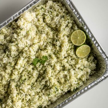 disposable steam table pan filled with cilantro lime rice topped with sliced limes.