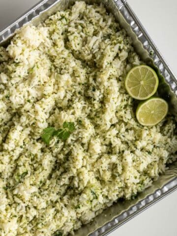 disposable steam table pan filled with cilantro lime rice topped with sliced limes.