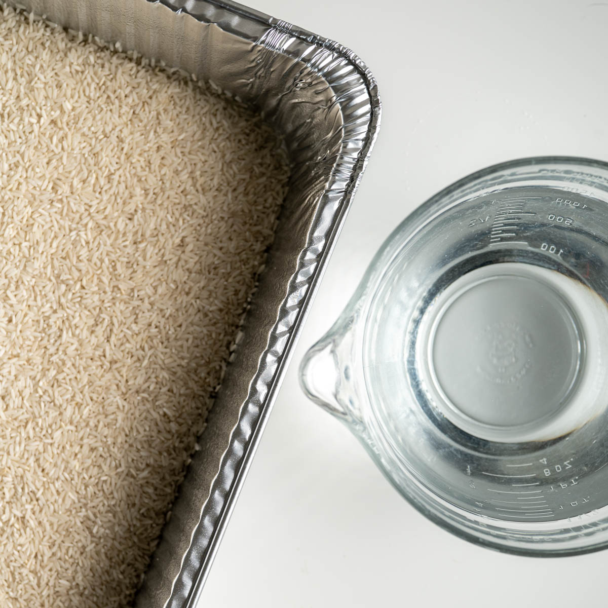 disposable steam table pan filled with long grain rice next to a large measuring bowl with water.