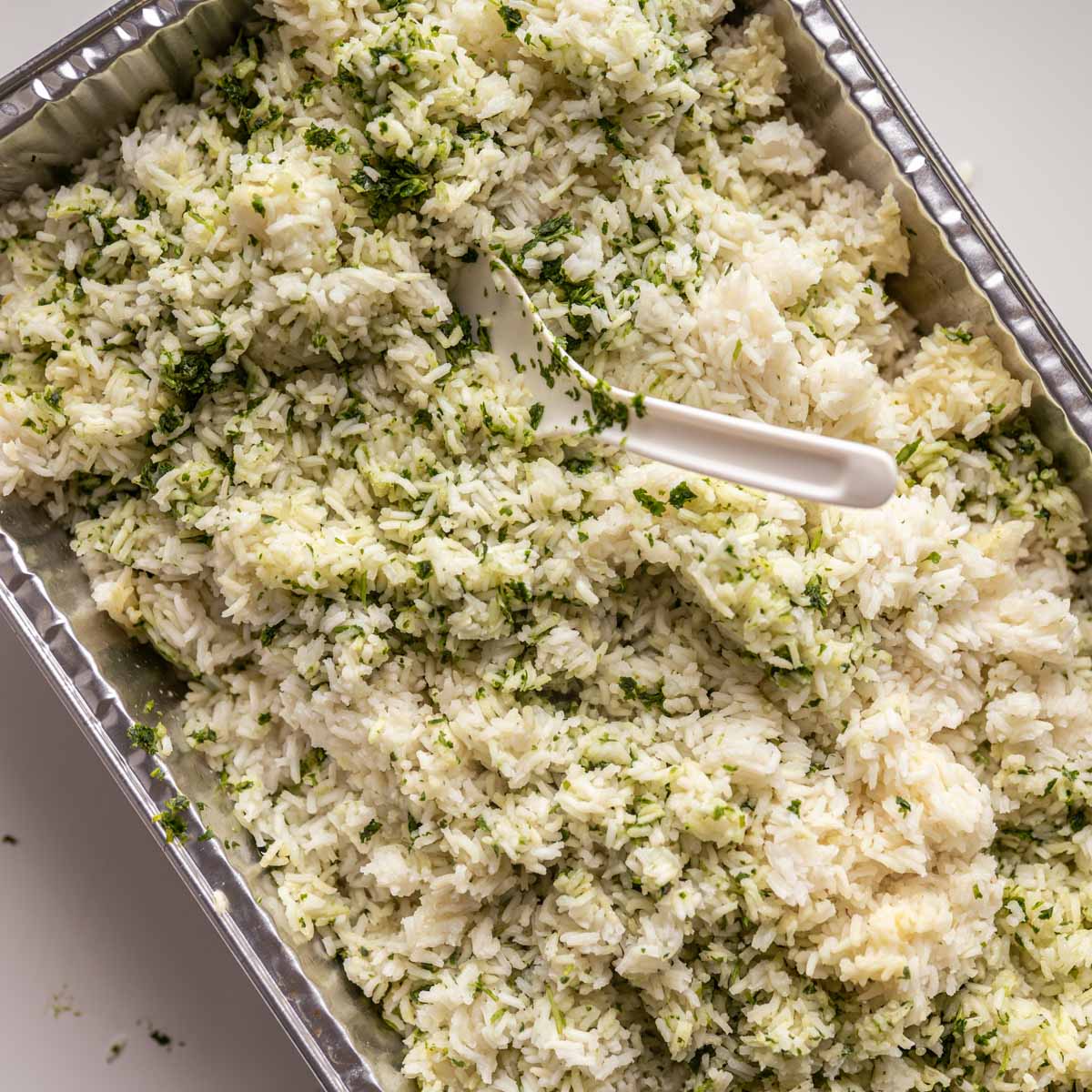 cooked white rice with the lime and lemon juice, chopped cilantro and additional oil being stired with a white rice paddle.