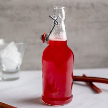 jar filled wtih rhubarb syrup with a glass of ice in the background.