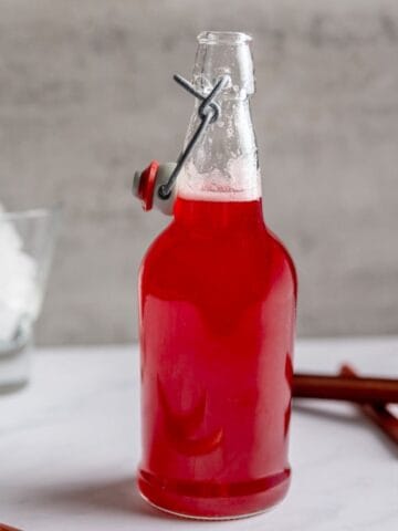jar filled wtih rhubarb syrup with a glass of ice in the background.