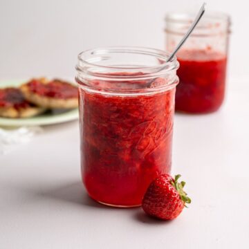 two jars of strawberry freezer jam with MCP with a toasted English muffin in the bakcground.