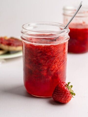 two jars of strawberry freezer jam with MCP with a toasted English muffin in the bakcground.