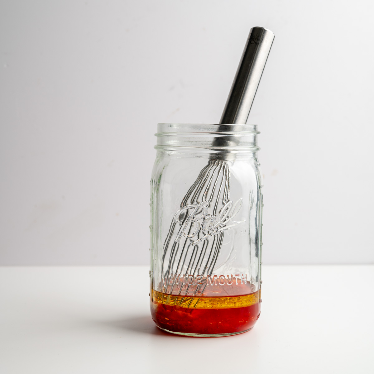 unmixed vinaigrette in a large mason jar with a whisk.