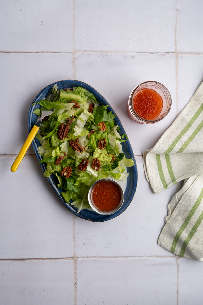 platter of lettuce topped with strawberry vinaigrette, pecans and fresh black pepper alongside a mason jar of dressing.