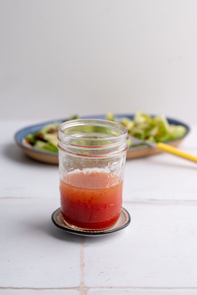 mason jar filled with strawberry vinaigrette in front of a platter filled with salad.