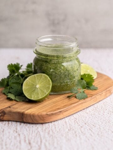 small jar filled with cilantro lime marinade on a wooden board with halved limes and fresh cilantro.