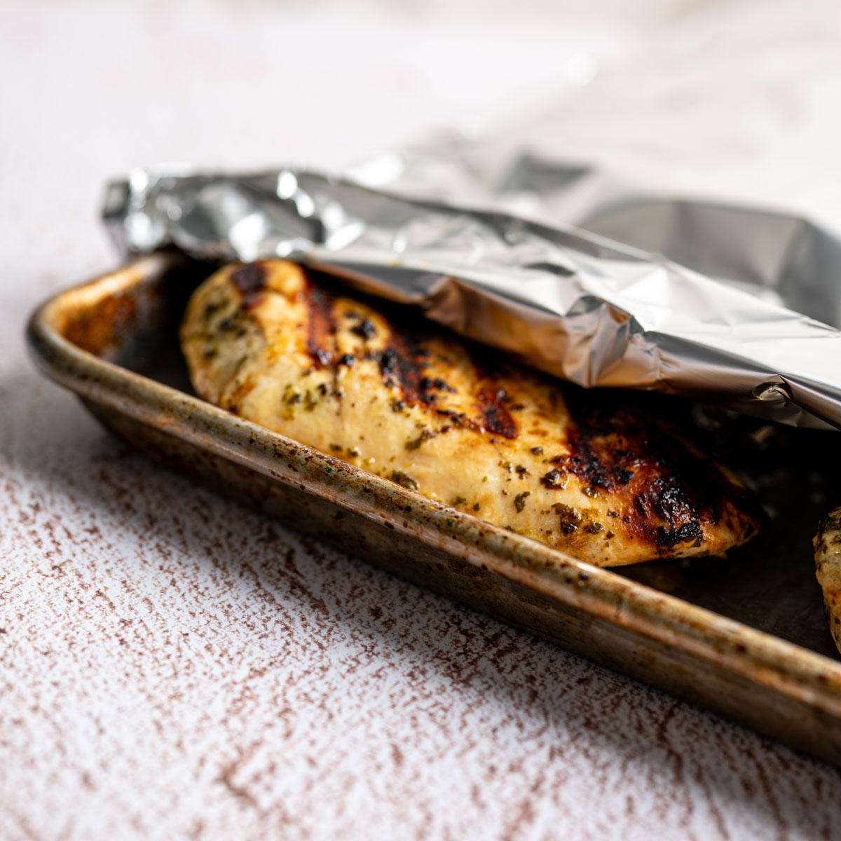 grilled chicken on a baking sheet covered in aluminum foil.