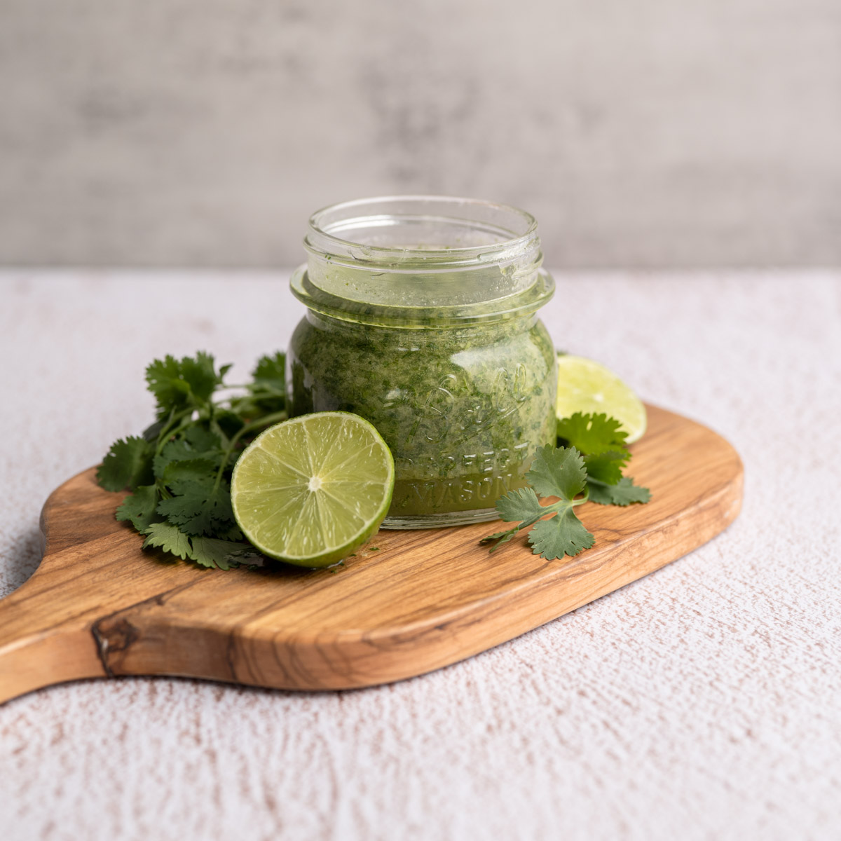 small jar of cilantro lime marinade on a wooden board, with halved limes and fresh cilantro. 