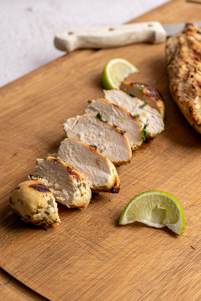 sliced chicken breast on a wooden board with a squeeze lime next to it.