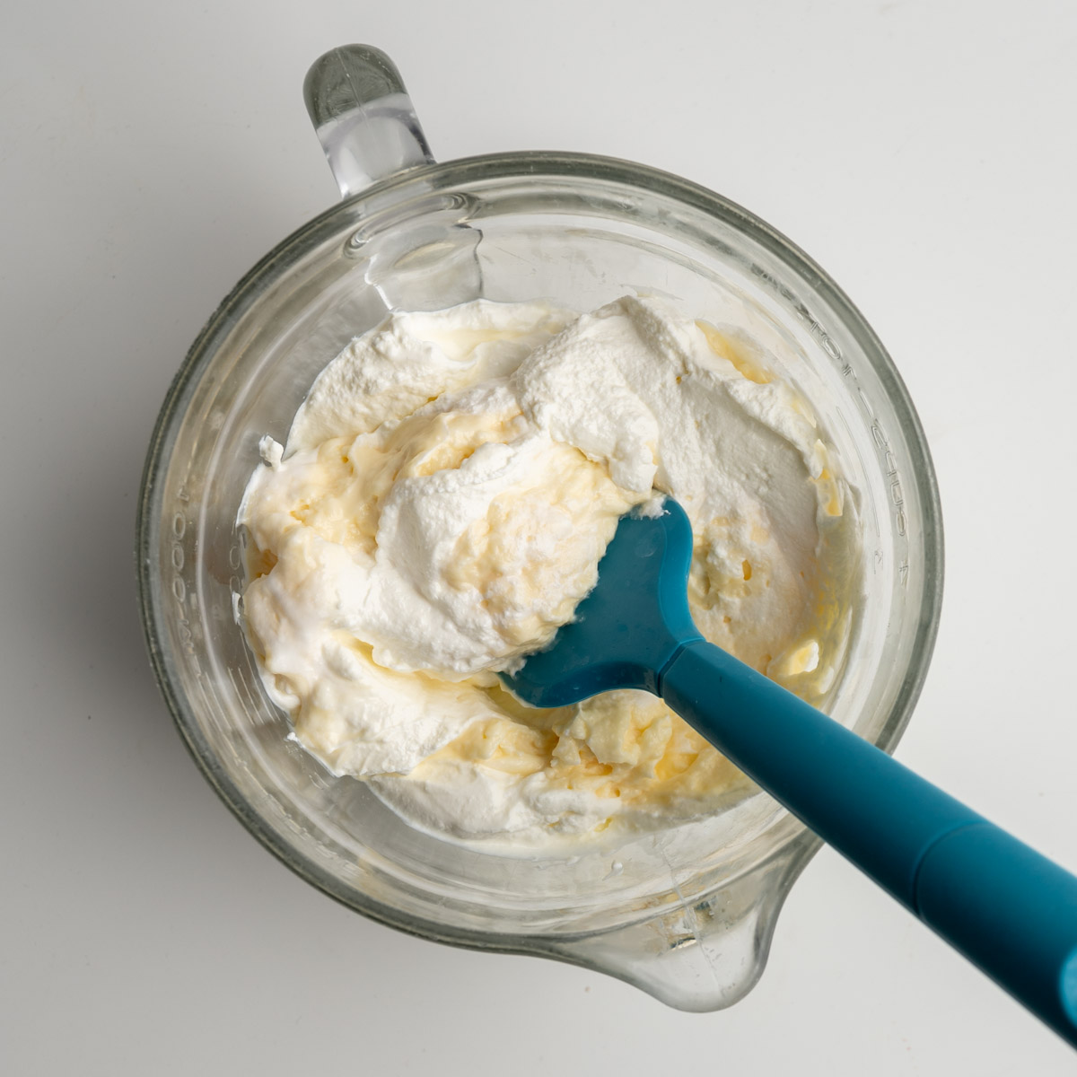 sour cream and mayonnaise in a glass bowl with a blue spatula.
