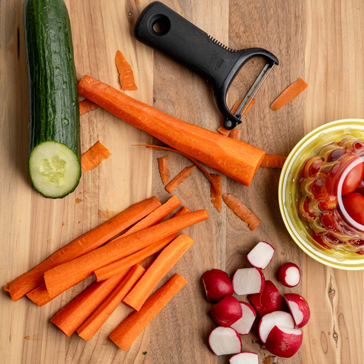 wooden board with fresh vegetables with a peeler and chopped vegetables.