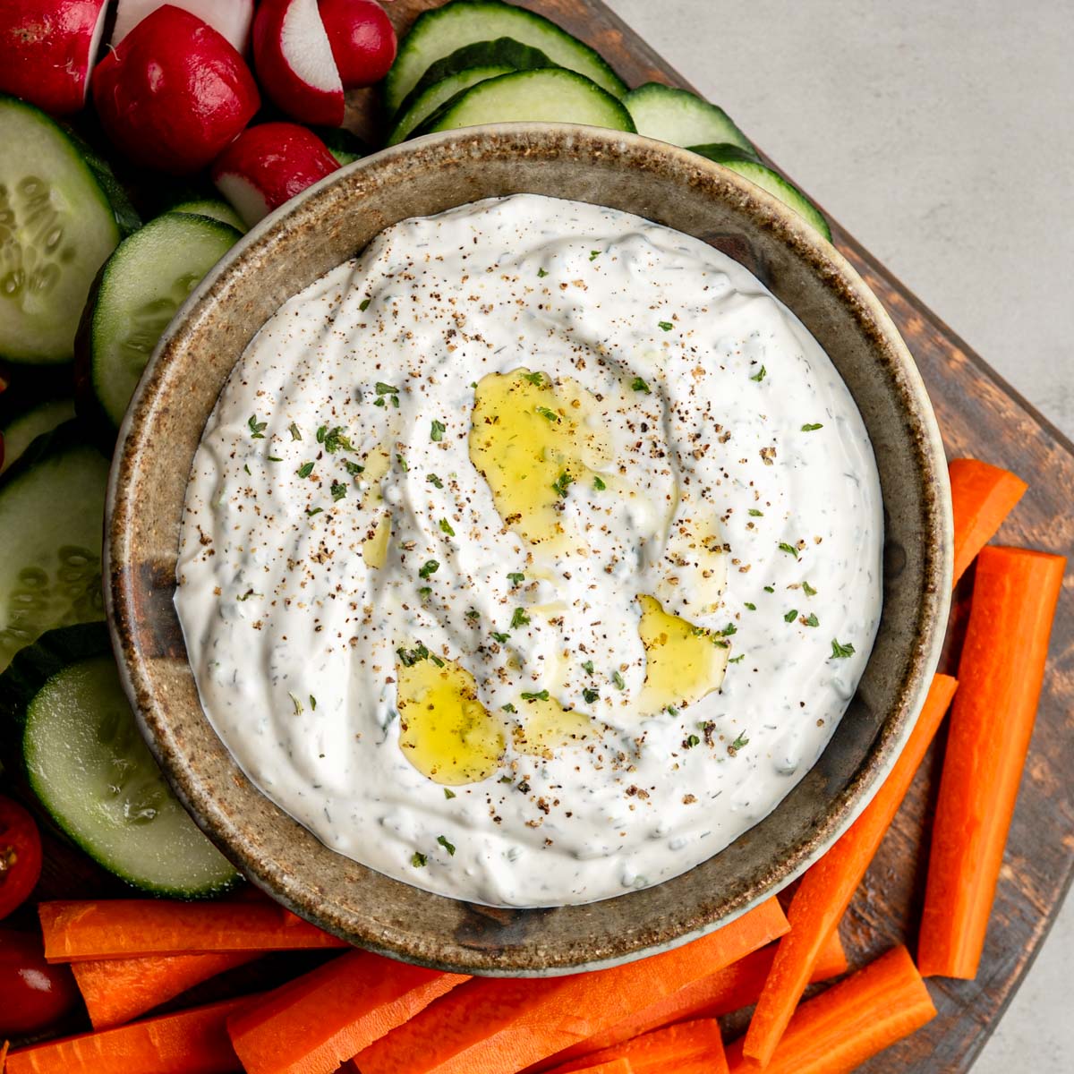 bowl of vegetable dip drizzled with garlic infused olive oil nestled among fresh vegetables. 