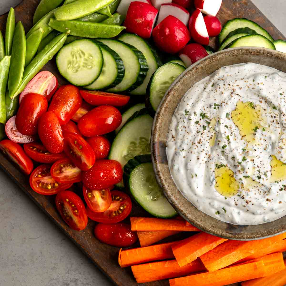 bowl of vegetable dip on a wooden board surrounded by fresh chopped vegetables.