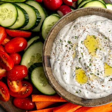 bowl of vegetable dip topped with garlic oil surrounded with fresh vegetables.