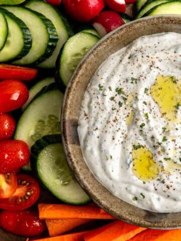 bowl of vegetable dip topped with garlic oil surrounded with fresh vegetables.