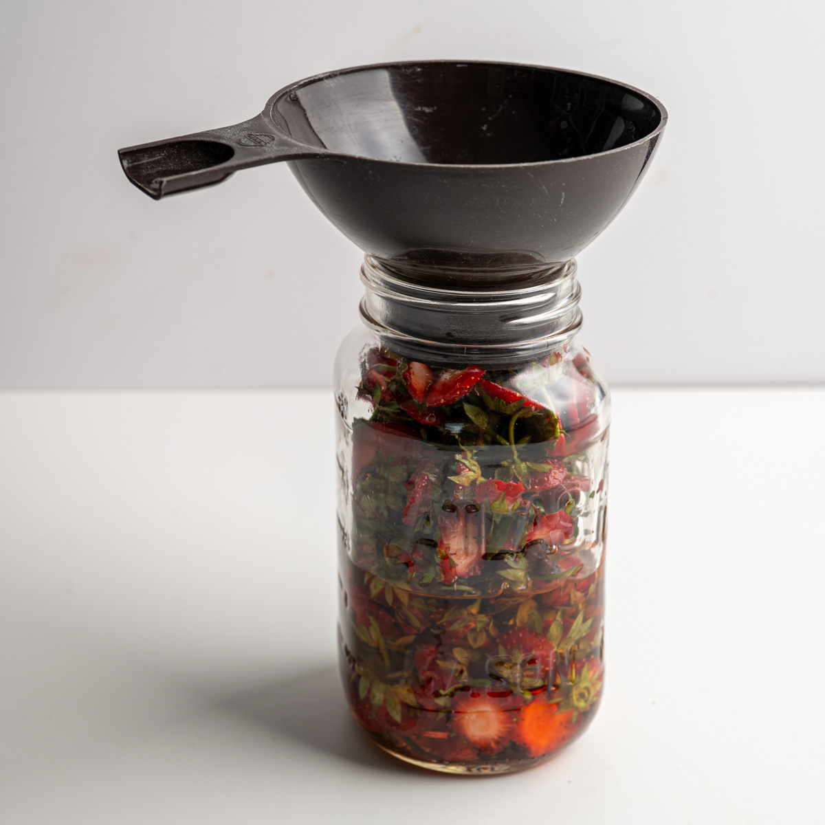 strawberry tops, vinegar in a large mason jar with a wide mouth funnel.