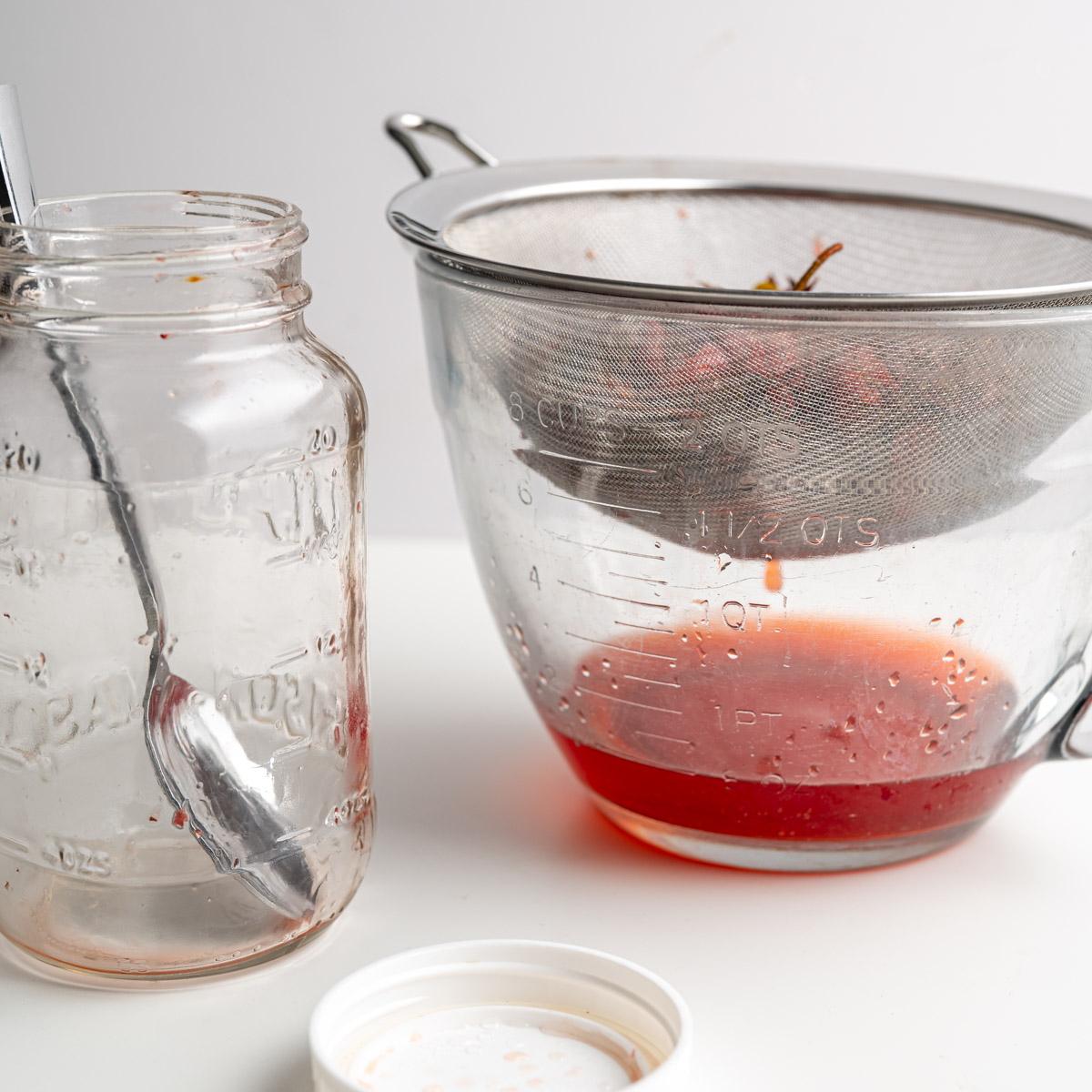 mesh strainer filled with strawberry tops with a bowl beneath catching the infused vinegar.