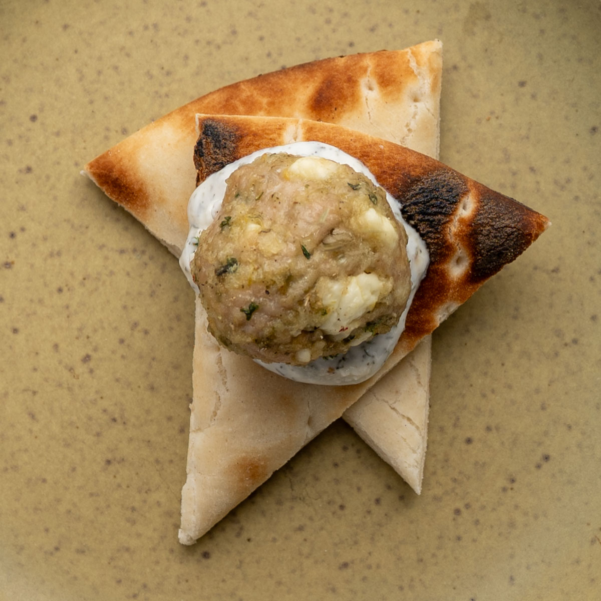 two pieces of pita bread topped with yogurt sauce and a greek chicken meatball.