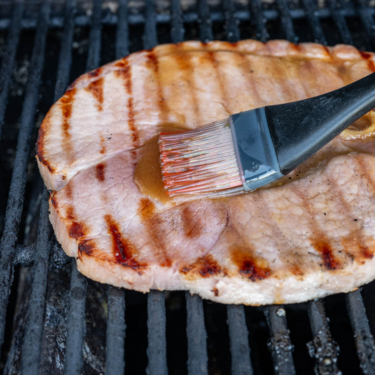 brushing glaze onto a grilled ham steak.