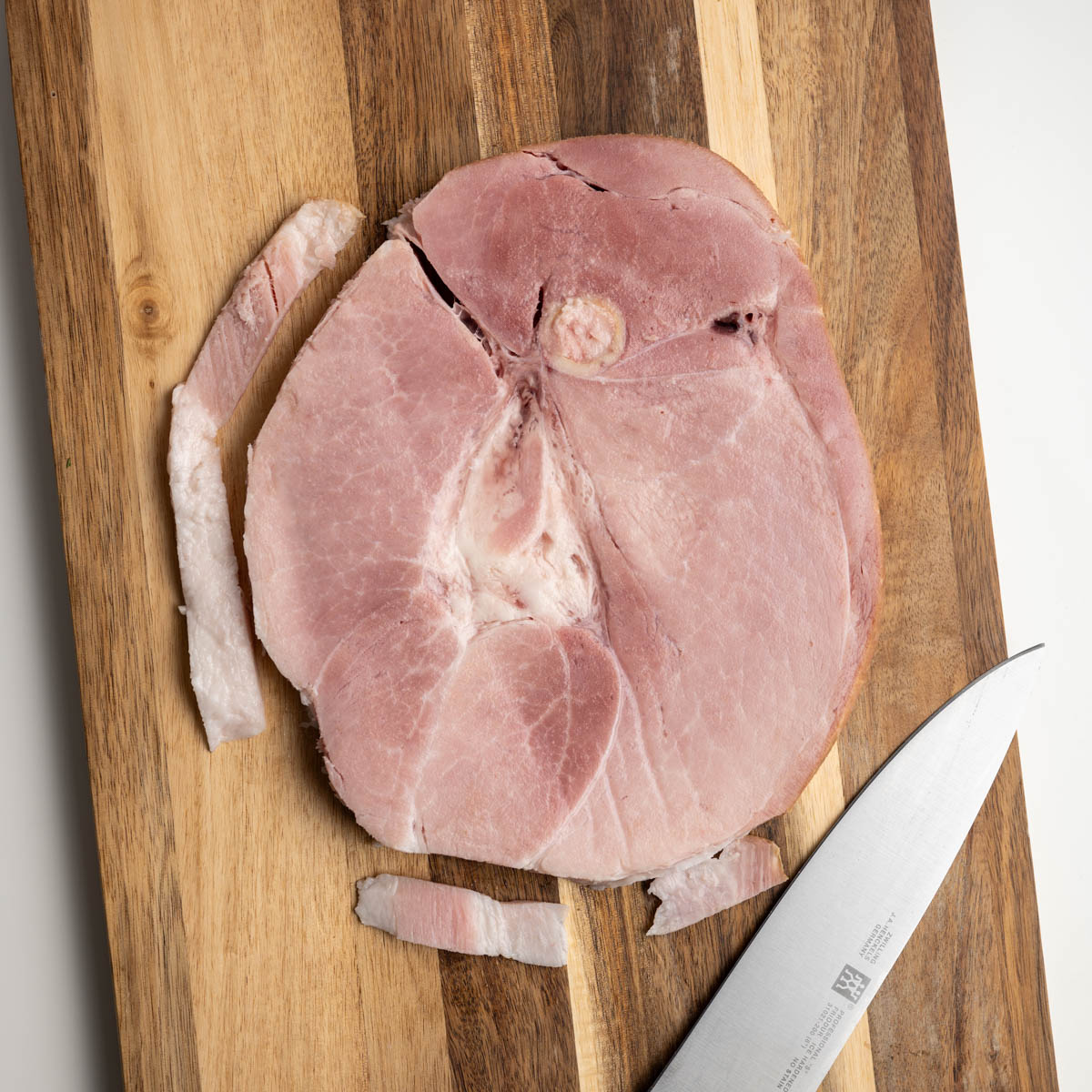 fat trimmed off a ham steak of a wooden cutting board.