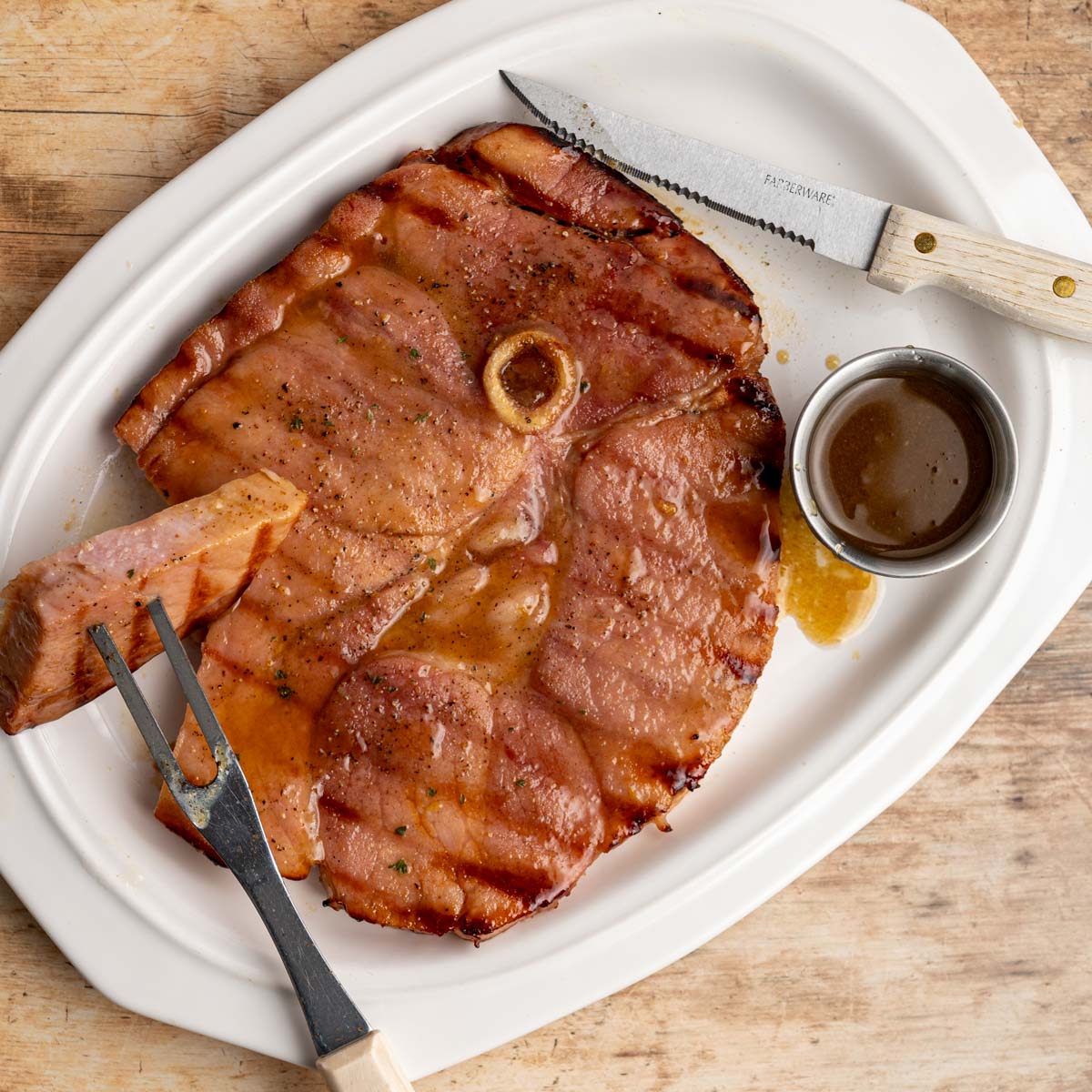 sliced grilled ham steak on a white platter with a dipping sauce. 