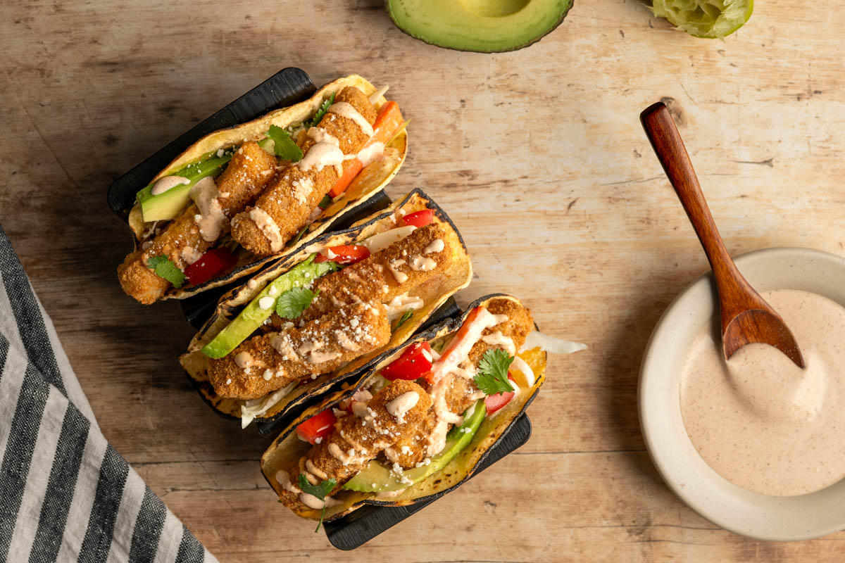 three fish tacos in a taco stand with a small dish of chipotle sauce.