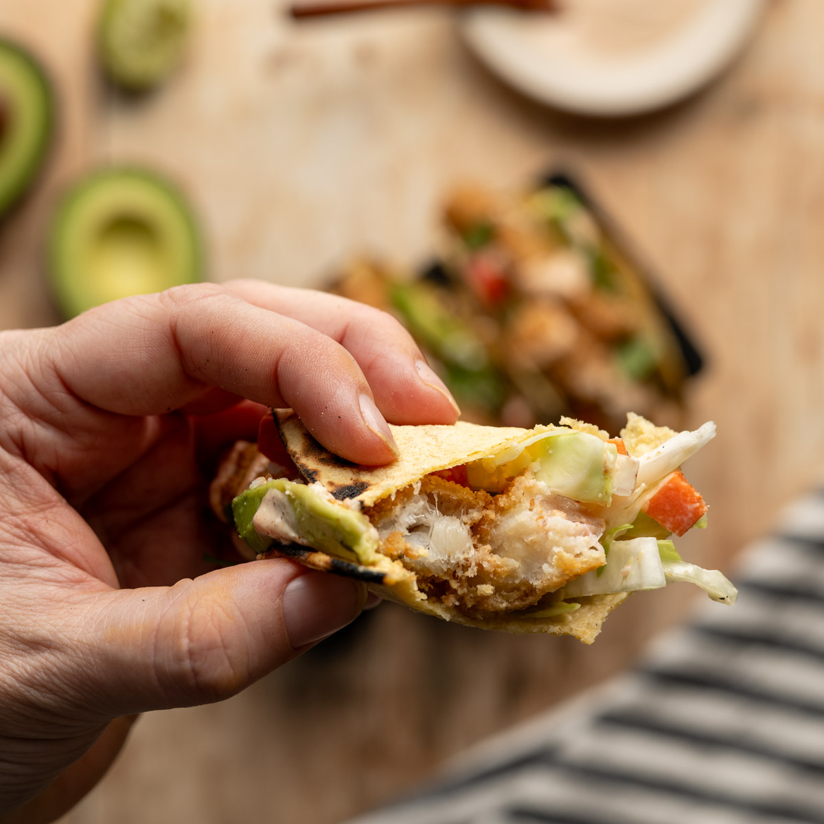 hand holding a fish stick taco with a bite missing.