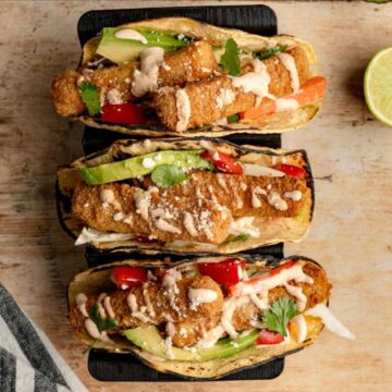 three fish stick tacos in a taco stand on a wooden board.