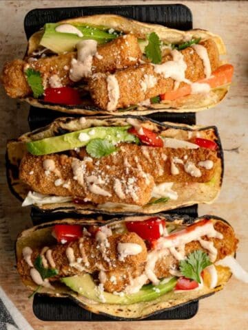 three fish stick tacos in a taco stand on a wooden board.