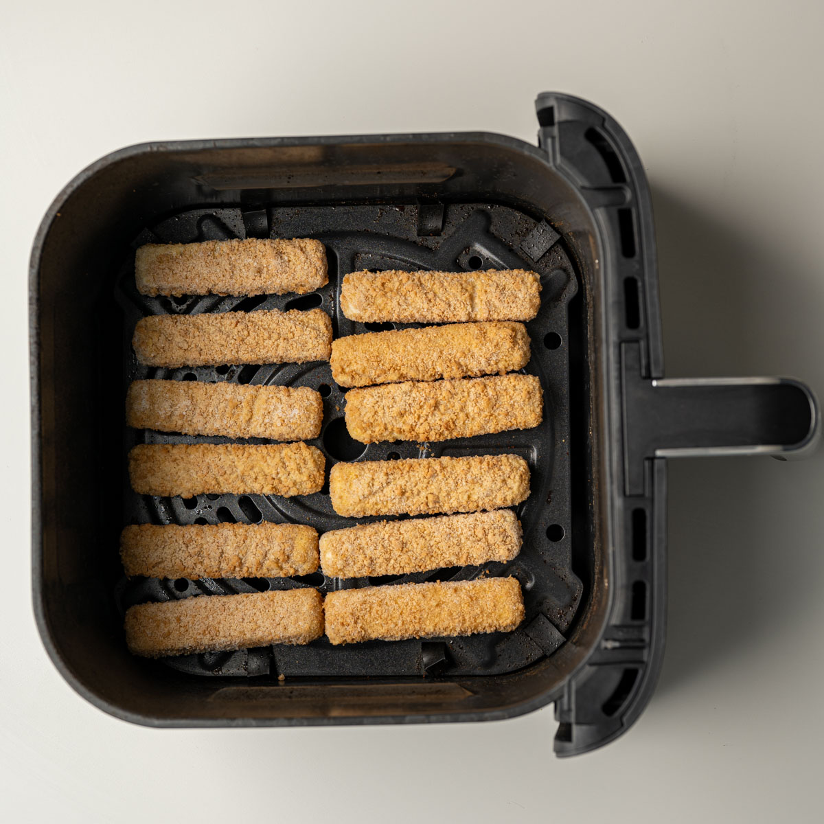 air fryer basked with a single layer of fish sticks.
