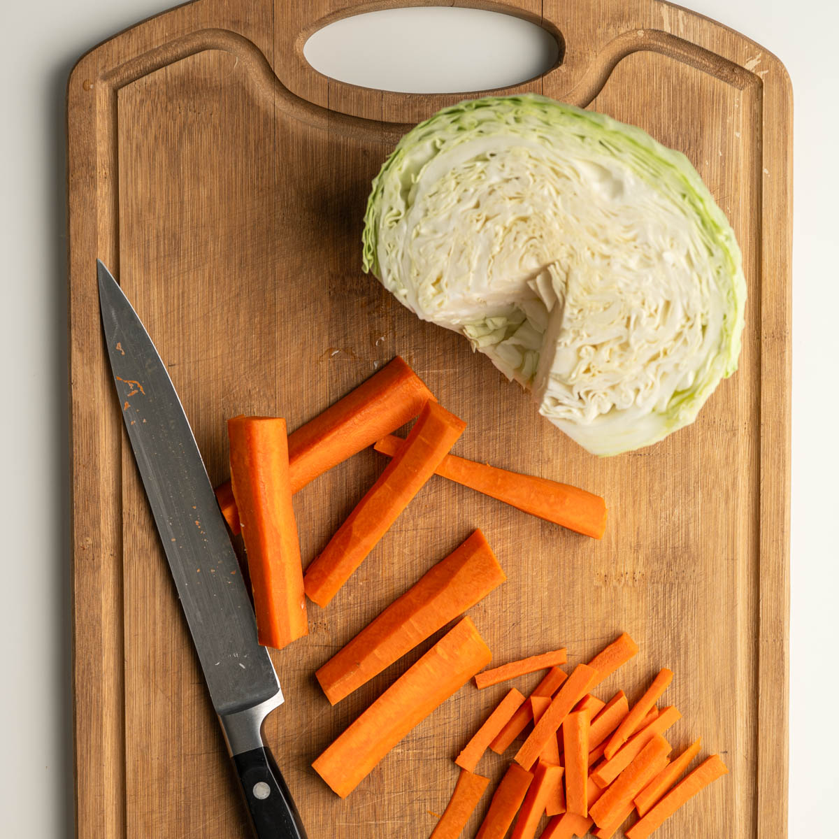 on a wooden cutting board with a cored cabbage and carrots.