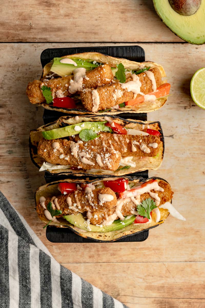three fish stick tacos in a taco stand on a wooden table.