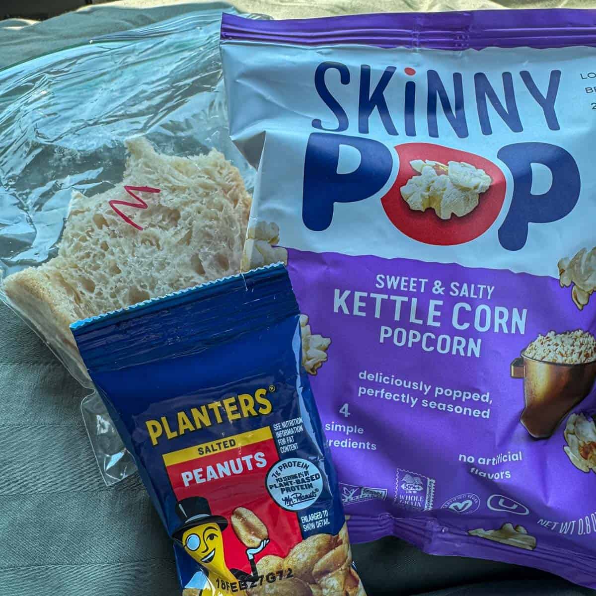 a bag of skinny pop, peanuts and a sandwich.