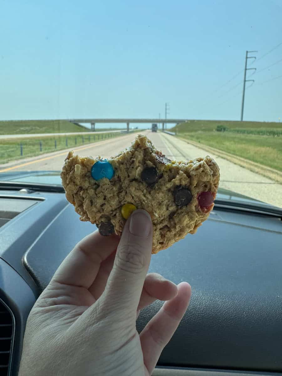 hand holding a monster cookie with two bites missing.