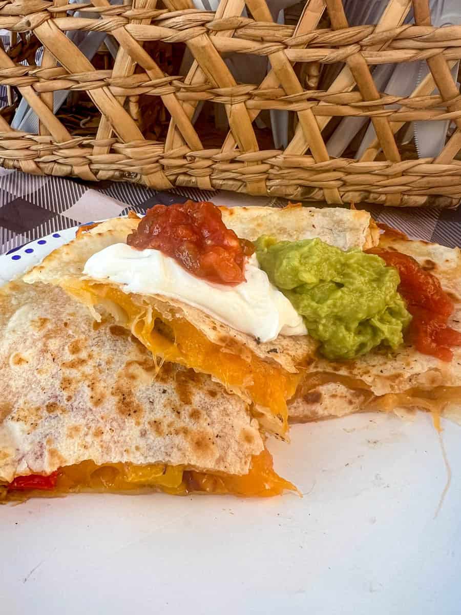 chicken quesadilla stacked on a paper plate topped with sour cream, salsa and guac.