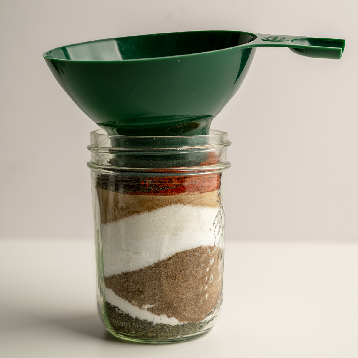 spices layer into a wide mouth mason jar with a funnel on top.